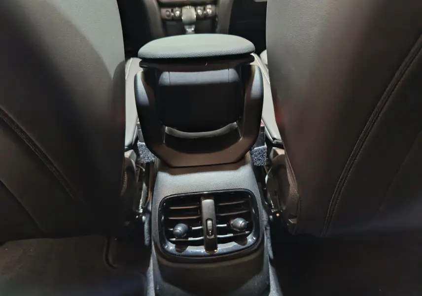 Détail des aérateurs arrière noirs entre les sièges avant en cuir foncé du MINI Countryman hybride blanc.