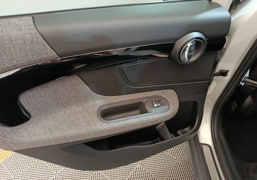 Gros plan sur la porte avant droite blanche du MINI Countryman Cooper SE avec habillage tissu gris et poignée chromée.