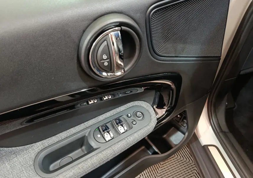 Gros plan sur la porte côté conducteur du MINI Countryman blanc, montrant les commandes de vitres et la poignée chromée.
