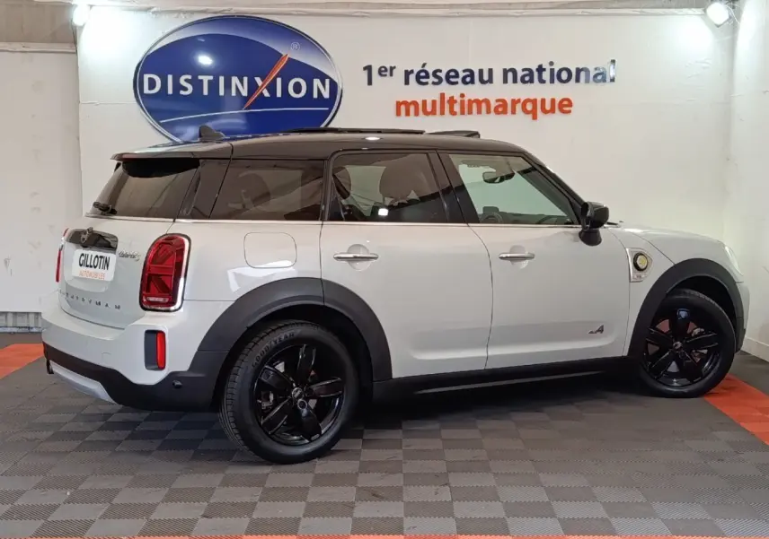 Vue latérale droite d'un MINI Countryman Cooper SE blanc avec toit noir et jantes noires en intérieur showroom.