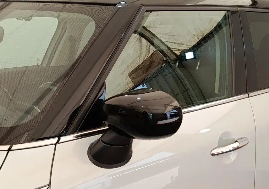 Gros plan sur le rétroviseur noir côté gauche d'une MINI Countryman blanche avec porte et vitre teintée.