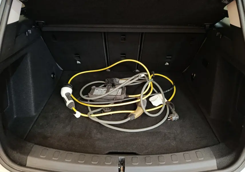 Coffre ouvert d'une MINI Countryman blanche 2021 montrant un câble de recharge hybride posé sur la moquette noire.