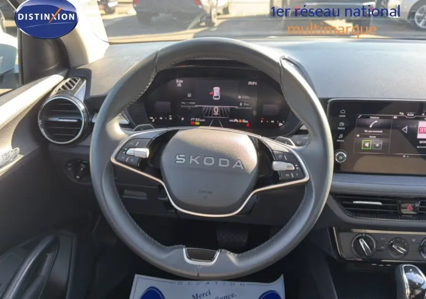 Vue intérieure centrée sur le volant SKODA avec tableau de bord numérique et écran tactile, ambiance moderne et épurée.
