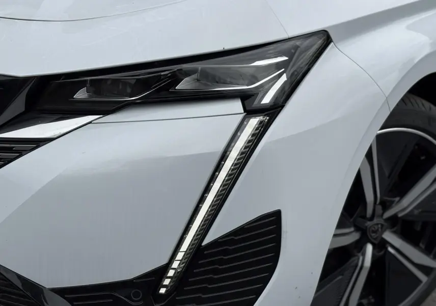 Gros plan sur le phare avant gauche blanc Okenite du Peugeot 308 2024 avec jante alliage 18 pouces diamantée.