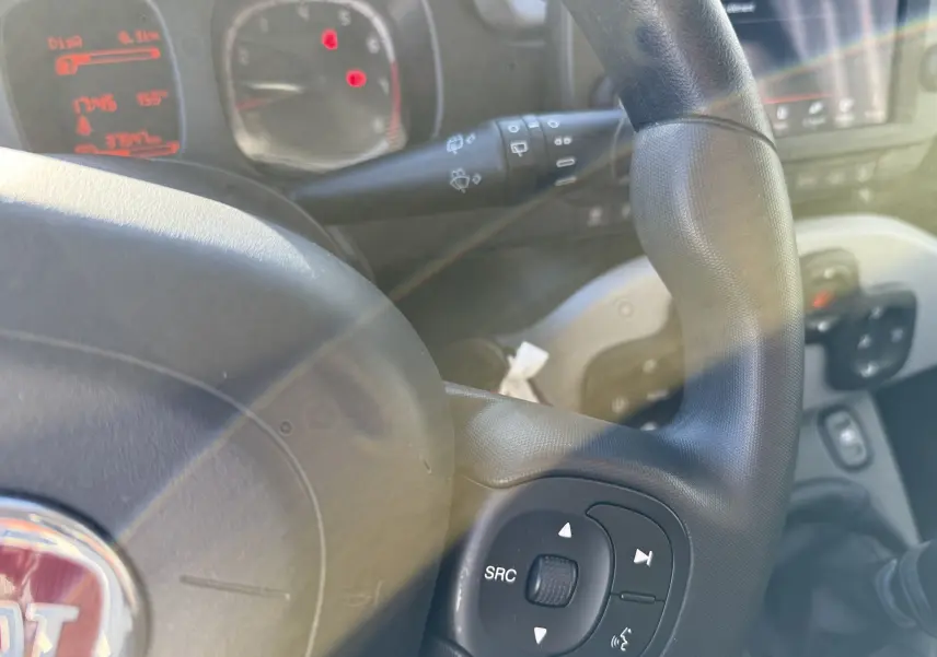 Gros plan sur le volant noir de la Fiat Panda City Cross 2023, avec commandes multimédia visibles et tableau de bord flou en arrière-plan.