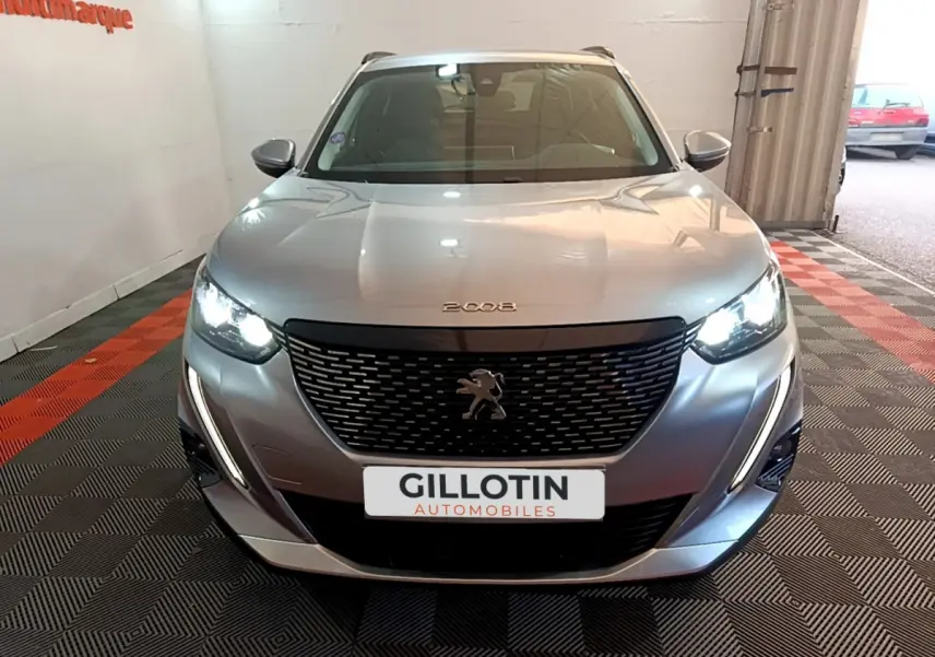 Vue frontale d'un Peugeot 2008 gris clair avec phares allumés et calandre noire distinctive.