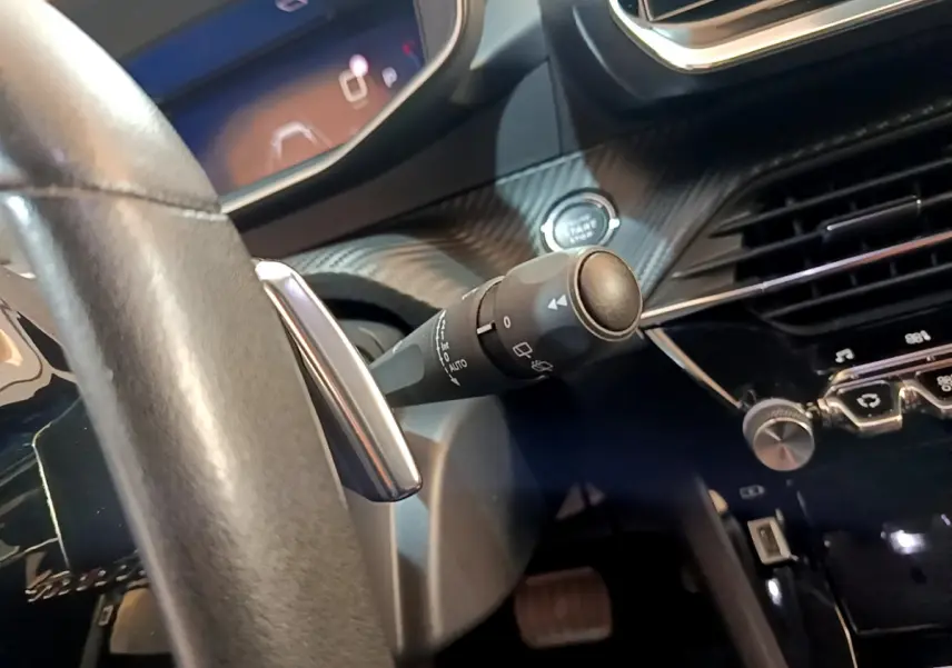 Gros plan sur la commande d'essuie-glace et le bouton start/stop du tableau de bord noir de la Peugeot 2008 gris clair.