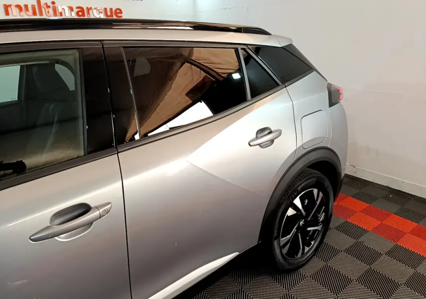 Vue côté droit arrière d'un Peugeot 2008 gris clair avec jante noire et toit noir contrasté dans un intérieur showroom.