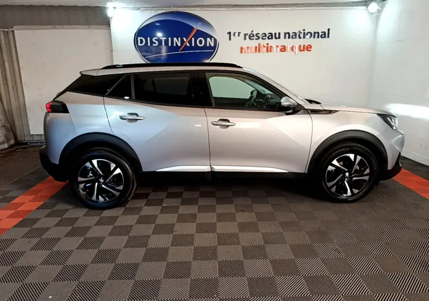 Profil côté gauche d'un Peugeot 2008 gris clair stationné en intérieur avec jantes noires et toit panoramique.