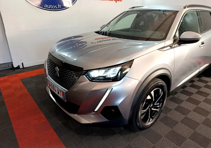 Peugeot 2008 gris clair vue 3/4 avant droit avec phares LED allumés et jantes noires brillantes.