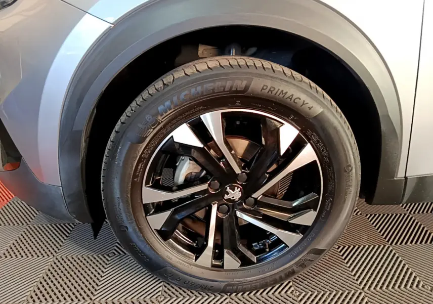 Gros plan sur la roue avant gauche gris clair du Peugeot 2008 avec jante noire et détails Michelin Primacy 4.