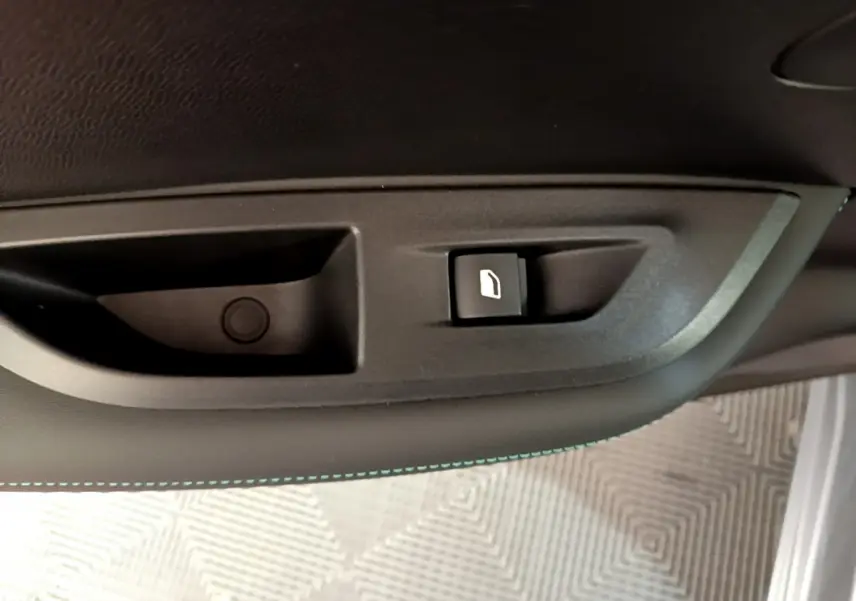 Bouton de déverrouillage de trappe à carburant sur la porte intérieure côté gauche d'un Peugeot 2008 gris clair.