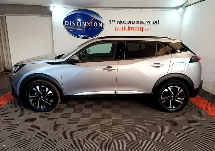 Profil côté gauche du Peugeot 2008 gris clair avec jantes noires et toit noir, en intérieur sur sol damier.