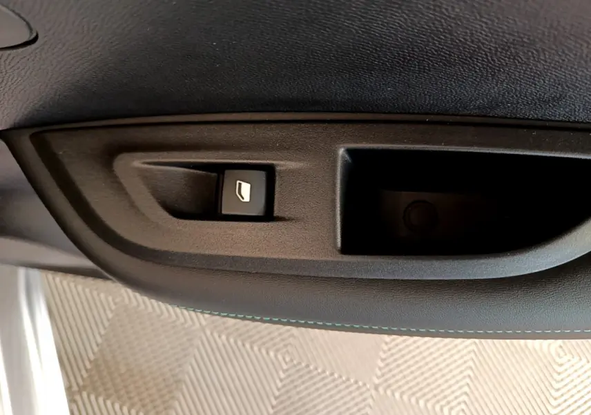Bouton de commande de lève-vitre sur la portière intérieure d'une Peugeot 2008 gris clair, vue rapprochée.