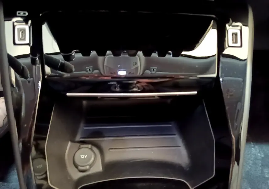 Prise 12V et rangement noir brillant dans l'habitacle du Peugeot 2008 gris clair, vue centrée en gros plan.
