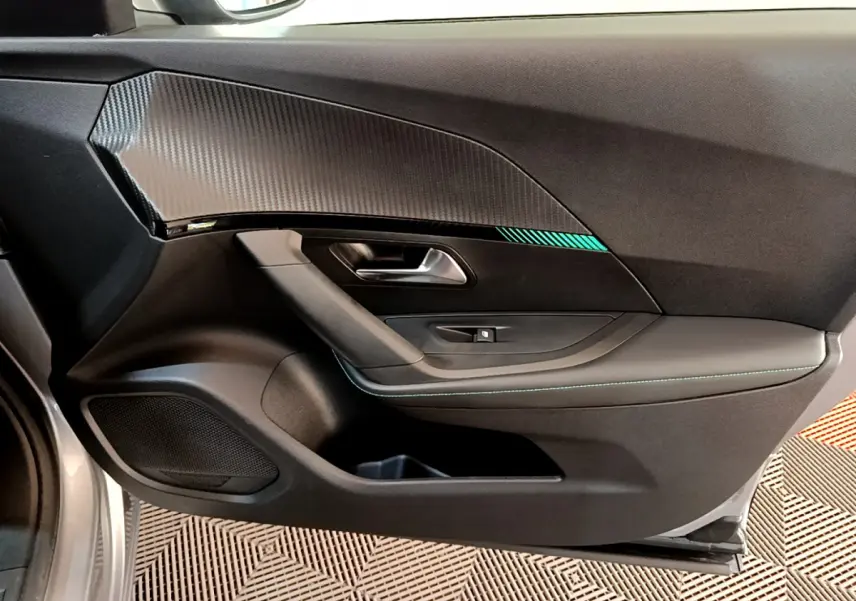 Vue intérieure côté gauche de la porte avant d'une Peugeot 2008 gris clair avec insert décoratif noir et surpiqûres vertes.