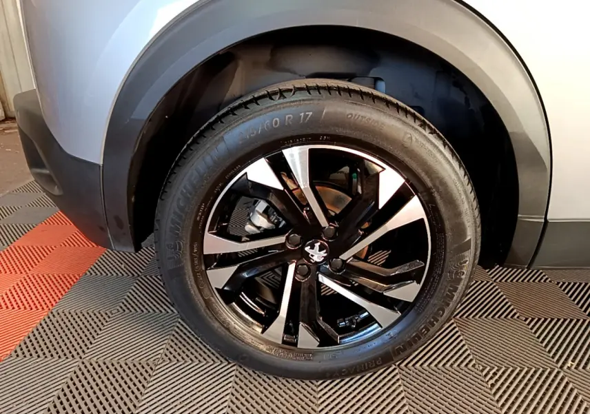 Gros plan sur la roue avant gauche du Peugeot 2008 gris clair, mettant en valeur la jante alliage noire et argentée.