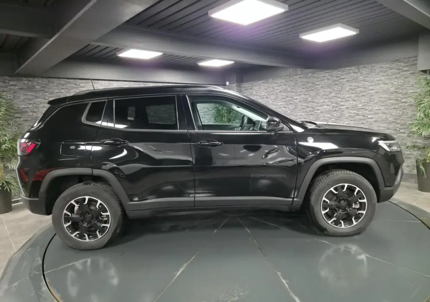Vue de profil côté gauche d'un Jeep Compass Trailhawk noir avec jantes alliage et stickers distinctifs en intérieur showroom.