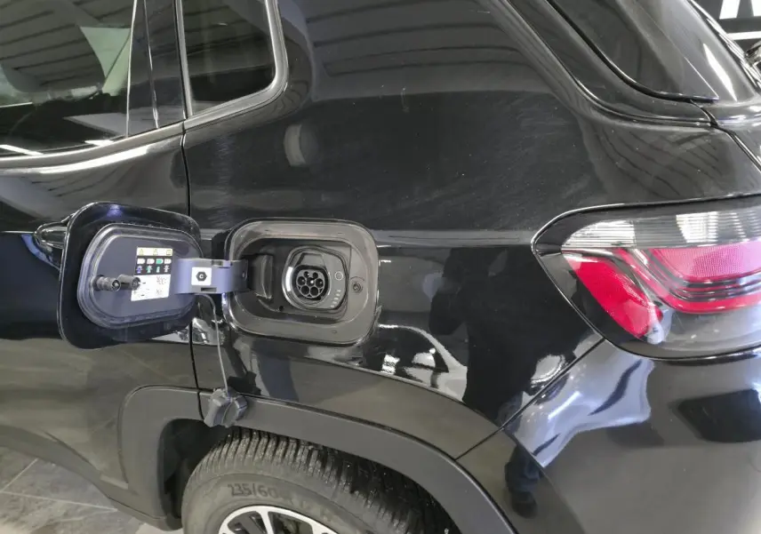 Prise de recharge ouverte côté gauche sur Jeep Compass Trailhawk noir 2024, avec feu arrière et jante visible.
