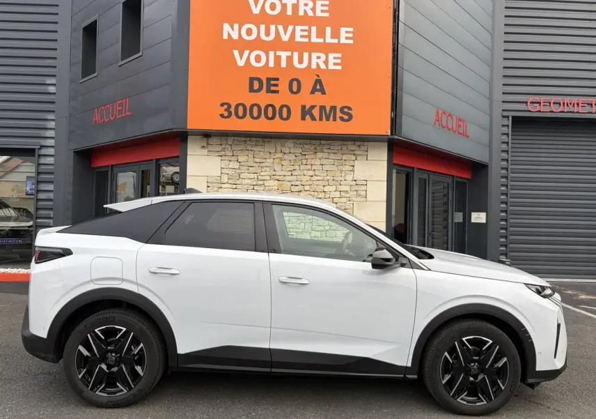 Vue latérale droite du Peugeot 3008 blanc 2026 avec toit noir et jantes noires devant un bâtiment commercial.