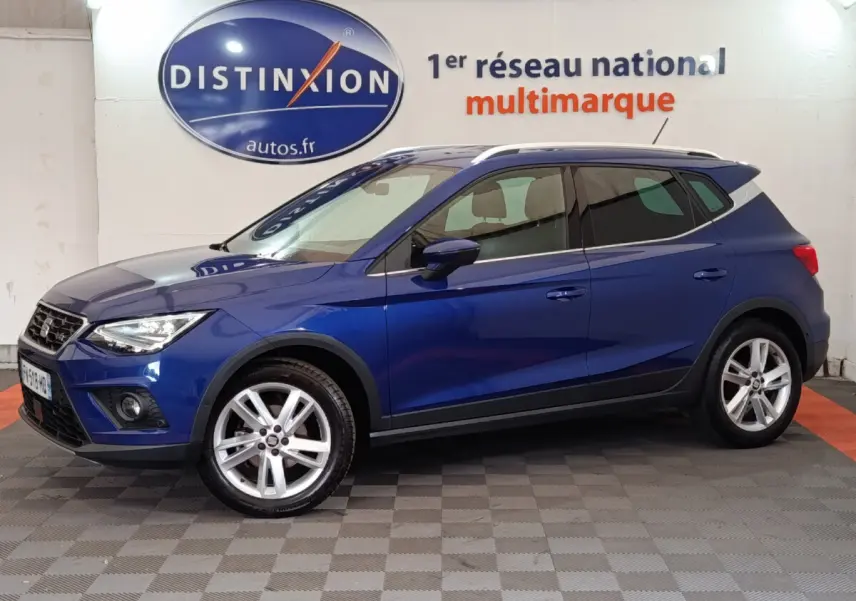SEAT Arona bleu en vue profil côté gauche, SUV compact avec jantes alliage et barres de toit chromées.