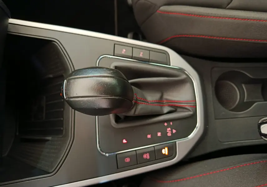Gros plan sur la console centrale de la SEAT Arona 2021, levier de vitesses automatique avec coutures rouges et sièges tissu noirs.