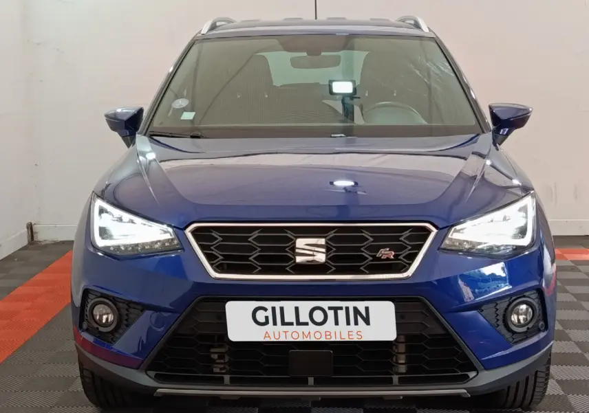 Vue frontale d'un SEAT Arona bleu 2021 avec phares LED allumés et logo FR sur la calandre noire.