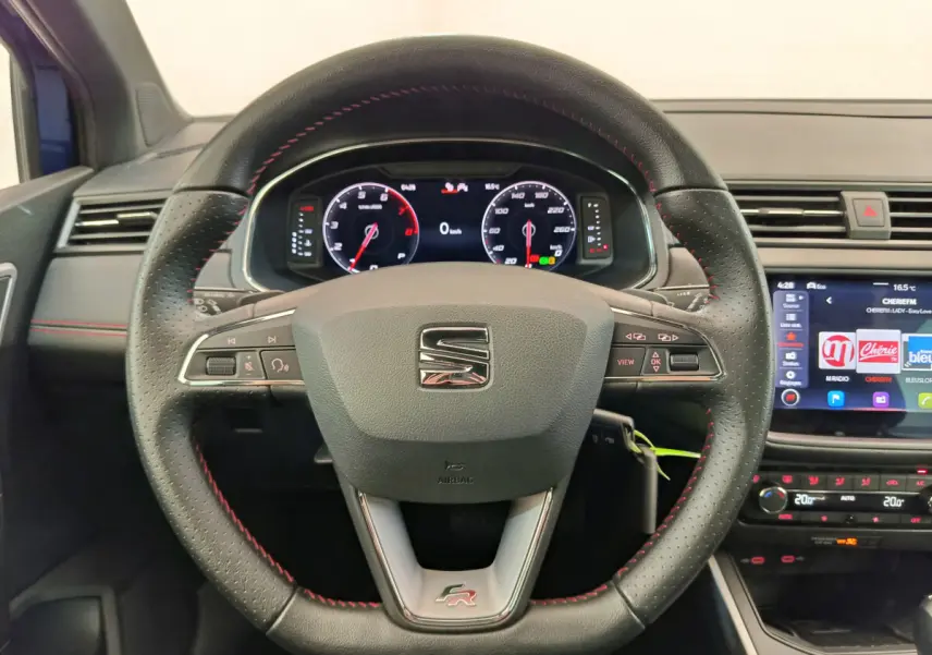 Vue intérieure centrée sur le volant cuir noir avec surpiqûres rouges du SEAT Arona FR 2021 et tableau de bord digital.