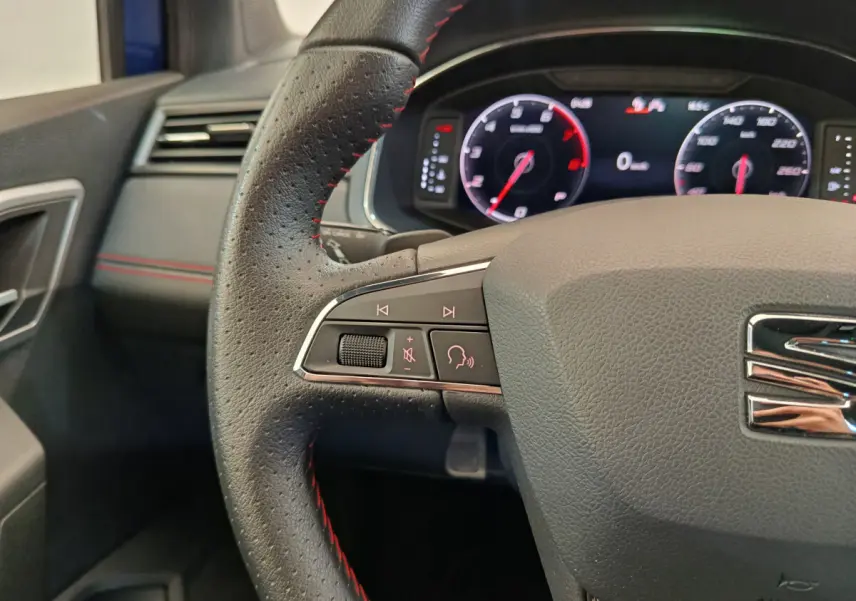 Gros plan sur le volant cuir noir avec surpiqûres rouges et tableau de bord numérique de la SEAT Arona 2021.