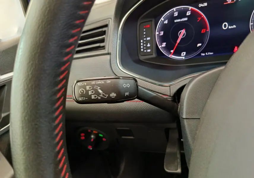 Gros plan sur la manette de régulateur de vitesse et le tableau de bord numérique du SEAT Arona 2021, intérieur noir avec surpiqûres rouges.