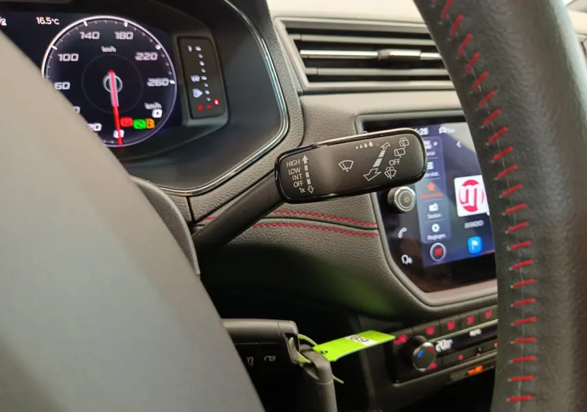 Vue rapprochée du commodo d’essuie-glace à gauche sur le tableau de bord noir avec surpiqûres rouges d’un SEAT Arona bleu 2021.