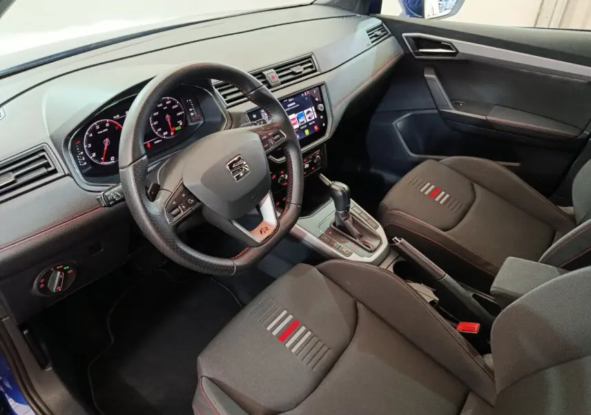 Intérieur du SEAT Arona 2021 vu côté conducteur, volant cuir, sièges noirs avec surpiqûres rouges et console centrale avec boîte auto.