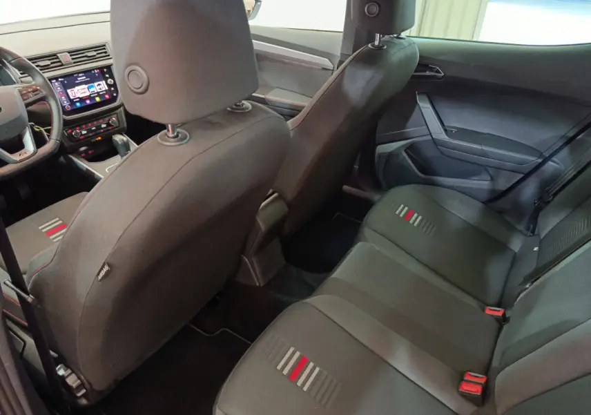 Vue intérieure arrière de la SEAT Arona 2021, sièges tissu noirs avec motifs rouges et gris, tableau de bord visible côté conducteur.