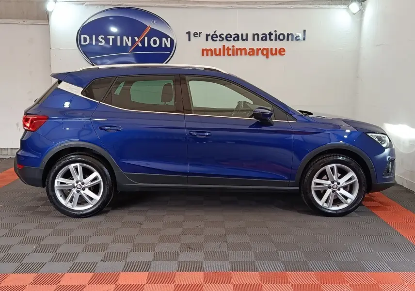 Profil côté gauche d'un SUV SEAT Arona bleu 2021 avec jantes alliage et toit noir en intérieur showroom.