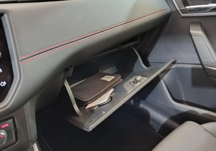 Vue intérieure côté passager du coffre à gants ouvert d'une SEAT Arona bleu 2021, avec surpiqûres rouges et pochette noire visible.
