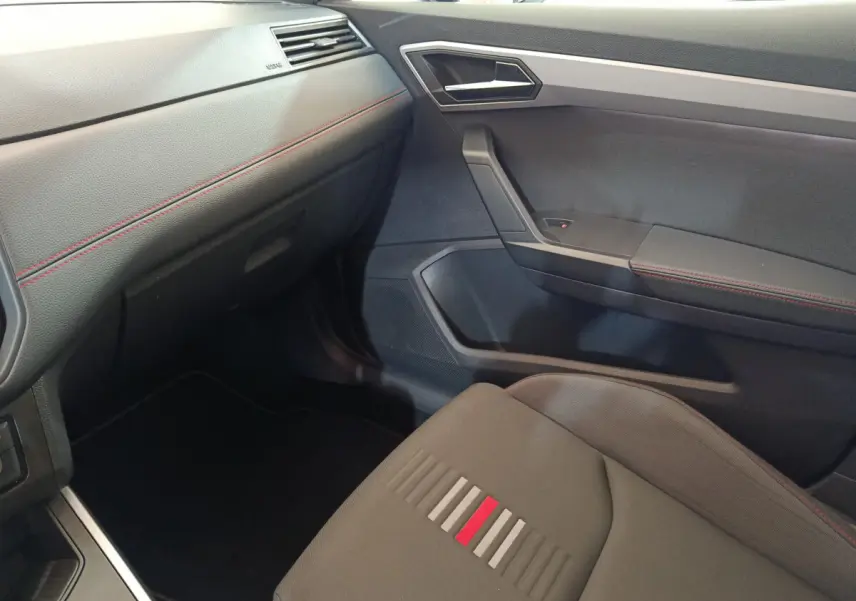 Intérieur côté passager de la SEAT Arona 2021, avec sièges gris et surpiqûres rouges, tableau de bord noir texturé.