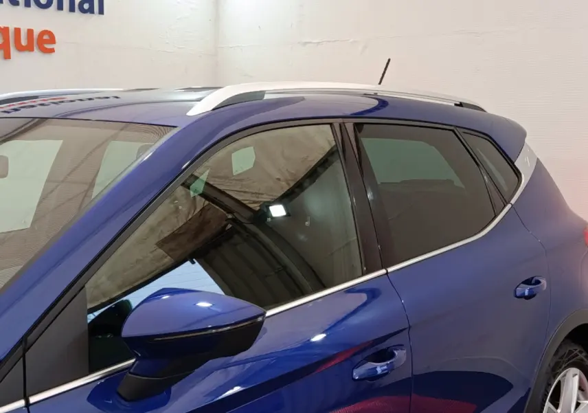 Vue de profil côté gauche du SEAT Arona bleu 2021, soulignant les rétroviseurs et barres de toit chromées.