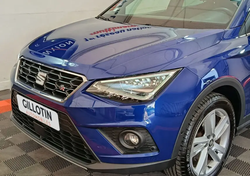 Vue 3/4 avant droite d'une SEAT Arona bleu profond avec calandre hexagonale et phares LED anguleux.