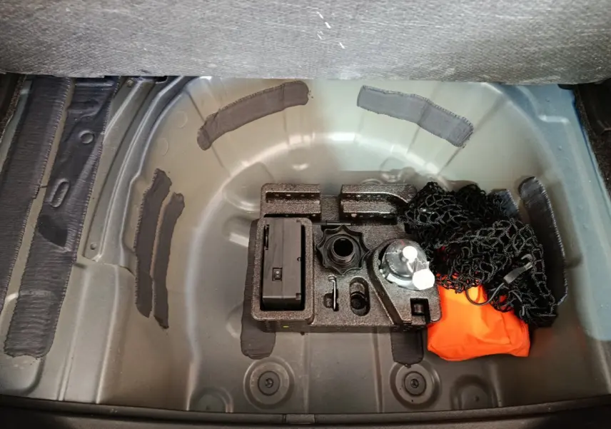 Vue plongeante sur le coffre vide d'une SEAT Arona bleu 2021, montrant le rangement sous tablette avec kit de bord.