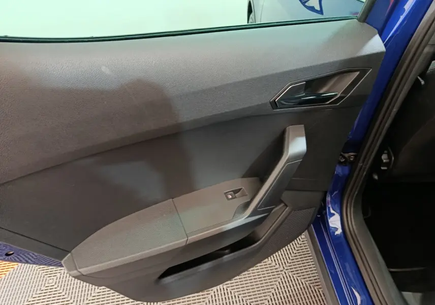 Vue rapprochée de la porte arrière gauche bleu vif d'une SEAT Arona 2021, avec poignée et commande de vitre noire.