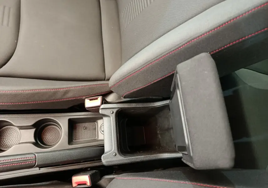 Vue plongeante sur la console centrale noire avec accoudoir ouvert et sièges tissu gris à surpiqûres rouges du SEAT Arona bleu 2021.