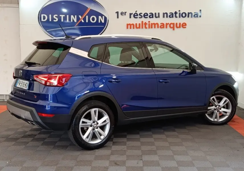 Vue latérale droite d'un SEAT Arona bleu 2021 avec jantes alliage et vitres teintées en showroom Distinxion.