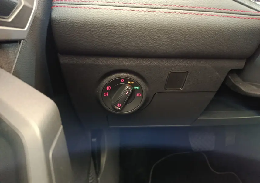 Gros plan sur le bouton de commande des phares du tableau de bord noir avec surpiqûres rouges d'une SEAT Arona bleu 2021.