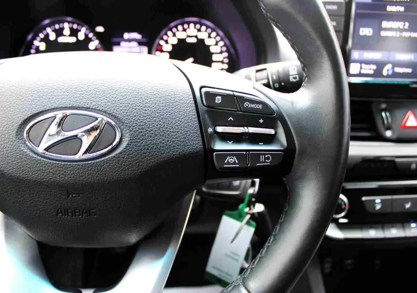 Gros plan sur le volant noir de la Hyundai i30 SW 2022 avec commandes intégrées et tableau de bord lumineux en arrière-plan.