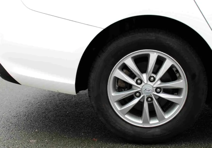 Gros plan sur la roue arrière droite d'une Hyundai i30 SW blanche polaire, mettant en valeur la jante alliage 15 pouces.