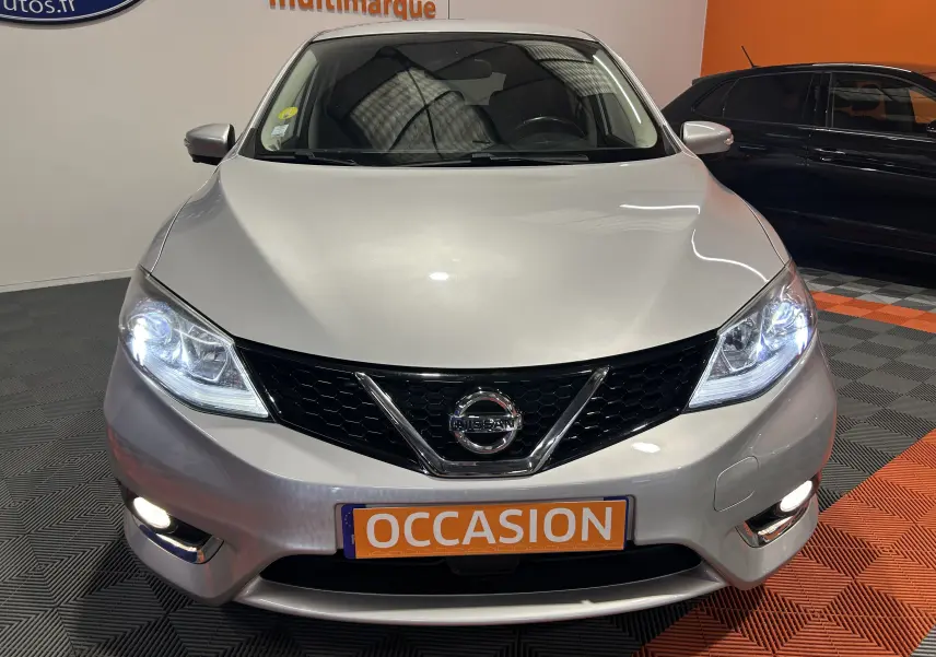 Vue avant d'une Nissan Pulsar gris métallisé avec phares allumés et plaque "OCCASION" en intérieur showroom.
