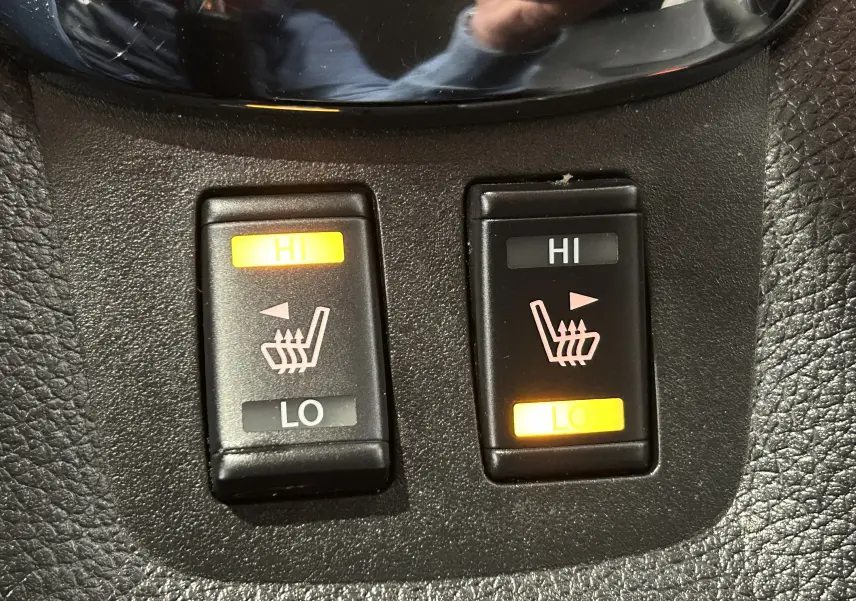 Gros plan sur les boutons de réglage des sièges chauffants, intérieur noir de la Nissan Pulsar gris 2018.