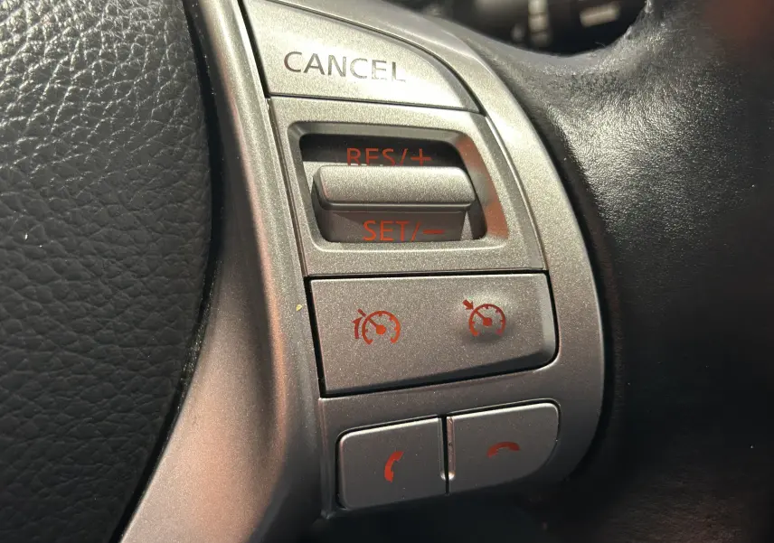 Gros plan sur les commandes argentées du volant noir de la Nissan Pulsar 2018, boutons de régulateur de vitesse et téléphone.