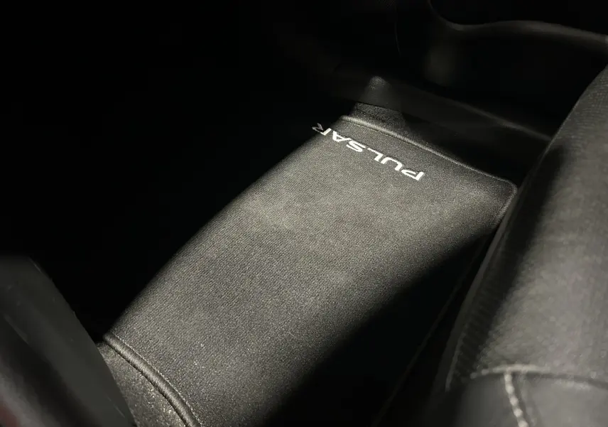 Tapis de sol noir avec inscription "PULSAR" en blanc, vue en plongée sur l'intérieur côté passager.