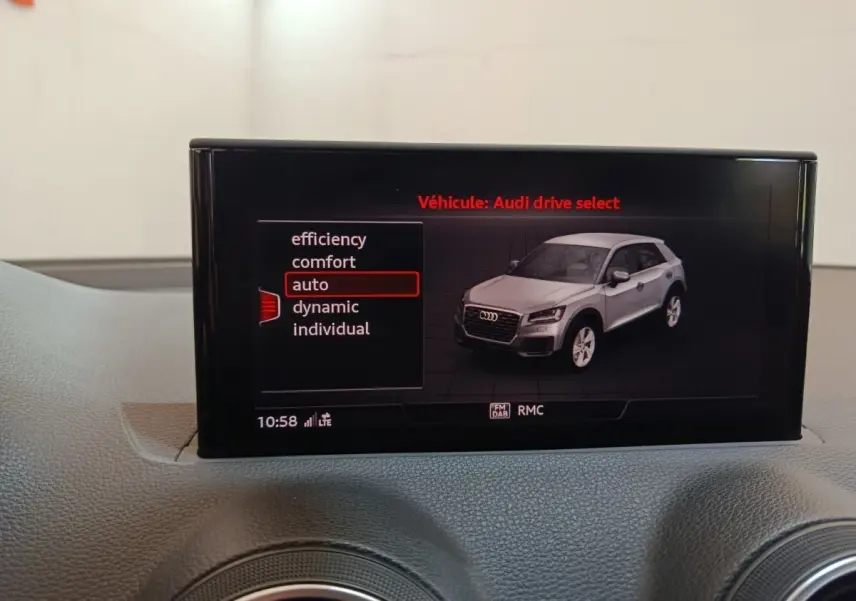 Écran tactile intérieur montrant une Audi Q2 gris clair en vue 3/4 avant droite avec modes de conduite sélectionnables.